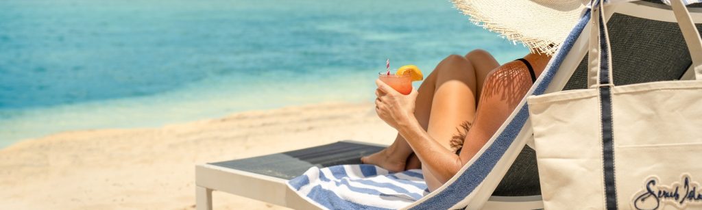 woman sitting in lounge chair on beach with orange drink in hand